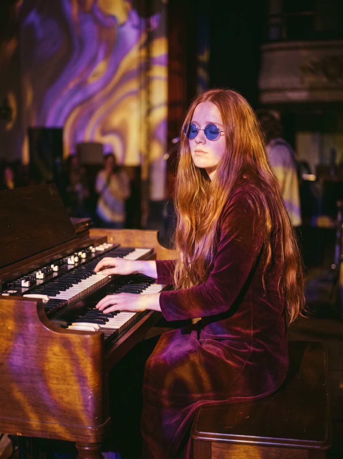 Juniper Lane, waist-length red hair and round blue sunglasses, plays a walnut organ in a velvet dress while purple and gold projected light swirls across her and the wall behind